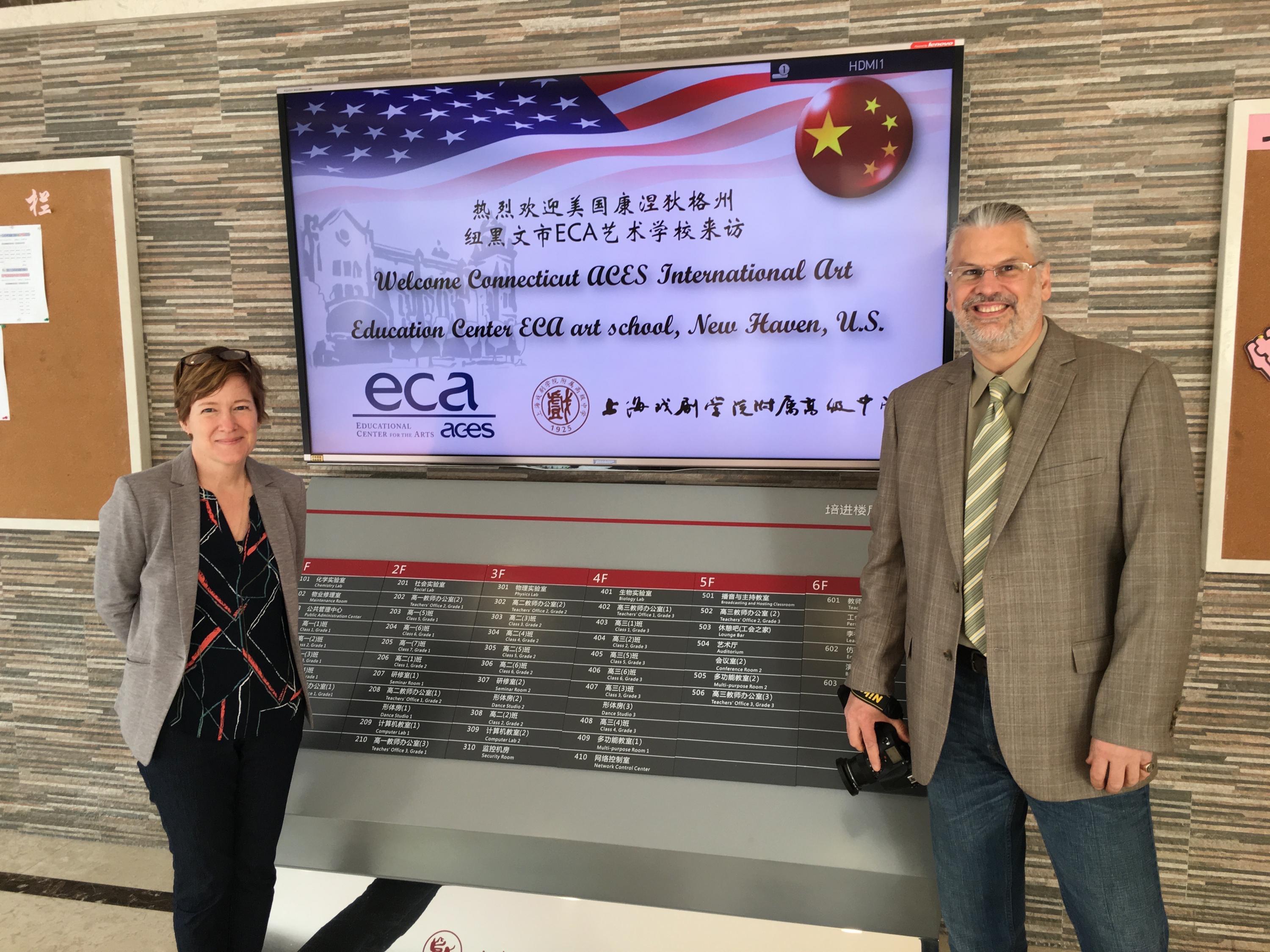 Two educators from the ACES ECA school take a picture in front of a screen welcoming them to China.
