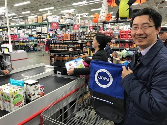 Visiting Scholars poses for a photo, holding up an ACES branded backpack in a grocery store.